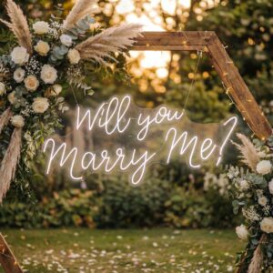 'Will You Marry Me?' neon sign displayed beneath a boho wooden arch with white pampas grass and floral arrangements in an outdoor garden setting