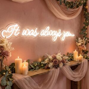 'It Was Always You' warm neon sign glowing above a romantic candlelit table with pink drapery and floral garlands