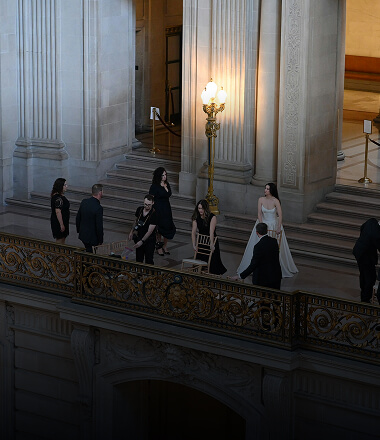 Elegant indoor proposal moment on a grand staircase in a classical NYC venue with onlookers and warm ambient lighting