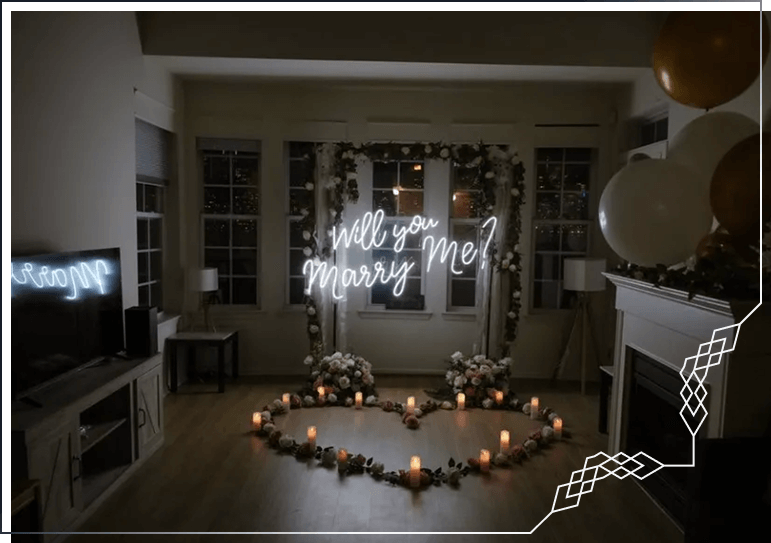 Indoor proposal setup with 'Will You Marry Me' neon sign, gold balloons, and candle-lit heart arrangement in an elegant living room
