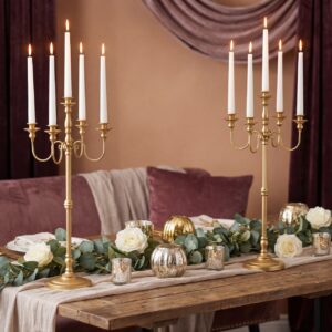 Gold five-arm candelabra with white taper candles on a wooden table with white roses and greenery garland for an elegant romantic proposal setting