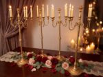Gold candelabra with white candles and pink rose garland on a draped dinner table with warm fairy lights for a romantic proposal atmosphere