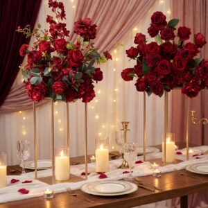 Lush red rose arrangement on a gold stand beside a place-setting dinner table with candelabras and mauve drapery for an intimate proposal dinner setup