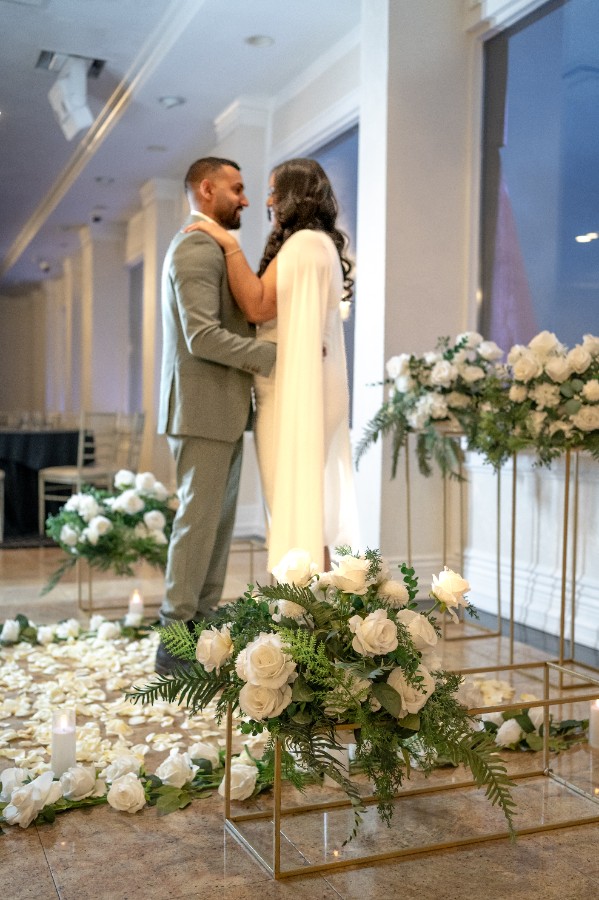 Couple standing before an elegant floral stand arrangement with white roses and greenery inside a bright modern venue for a romantic proposal
