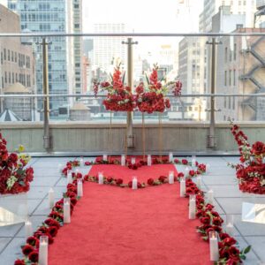 Red carpet proposal pathway with LED pillar candles and red floral arrangements on a rooftop terrace overlooking the Manhattan skyline on a clear day