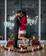 Couple embracing after a successful marriage proposal surrounded by a silk rose heart arrangement and candles with the illuminated NYC skyline behind them