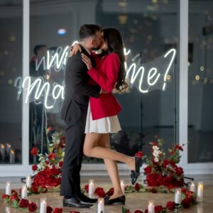 Couple embracing after a successful marriage proposal surrounded by a silk rose heart arrangement and candles with the illuminated NYC skyline behind them