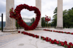 Red rose heart arch rental setup at a stone colonnade outdoor venue with red rose petals scattered on the ground for a romantic proposal