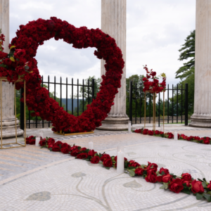Red rose heart arch rental setup at a stone colonnade outdoor venue with red rose petals scattered on the ground for a romantic proposal