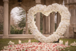 White floral heart arch at a stone garden colonnade with rose petals and candles for an elegant outdoor proposal