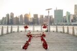 Rose petal pathway curving along a wooden pier overlooking Lower Manhattan and the East River at golden hour